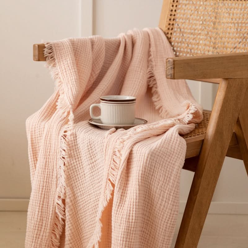 Pale pink Four-Layer Waffle Weave Cotton Throw Blanket draped on a chair with a cup.